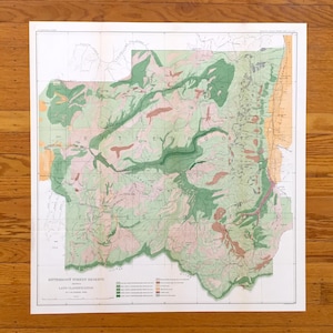 May include: A detailed land classification map of the Bitterroot Forest Reserve, featuring green, pink, and tan colours. The map is printed on white paper and is displayed on a wooden surface.