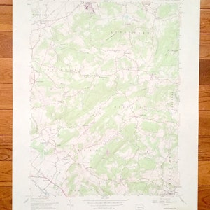 May include: A detailed topographic map with contour lines, roads, and place names. The map features shades of green and white, with text indicating the area's name and survey details. The map is printed on a white paper.