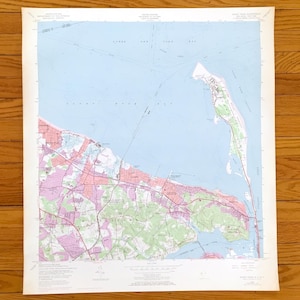 Può includere: Una carta topografica dell'United States Geological Survey di Sandy Hook, New Jersey, con acqua azzurra, aree urbane rosa e sezioni boschive verdi. La mappa include dettagliati segni cartografici, etichette di testo e linee di griglia.