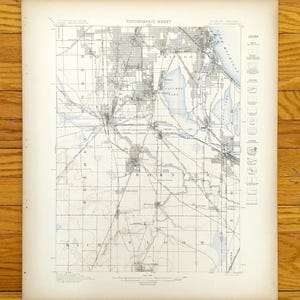 Pode incluir: Um mapa topográfico vintage com uma representação detalhada de uma cidade, provavelmente Chicago, e seus arredores. O mapa usa um sistema de grade e inclui rótulos de texto, características de água e uma legenda. O mapa é impresso em papel envelhecido.