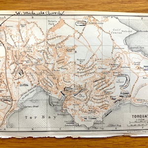 May include: A vintage map of Torquay, England, with a grid pattern and detailed street names. The map shows the location of St. Michael's Church, Victoria Park, Golf Course, Walls Rill, and other landmarks. The map is printed on a cream-colored paper with black and brown ink.