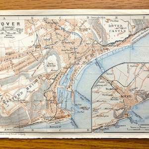 Puede incluir: Un mapa vintage de Dover, Inglaterra, con una escala de 1:20.000. El mapa muestra las calles de la ciudad, los puntos de referencia y las áreas circundantes, incluido el castillo de Dover y el Canal de la Mancha.