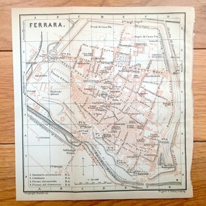 Puede incluir: Un mapa vintage de Ferrara, Italia, impreso en blanco y negro con resaltados rojos. El mapa muestra las calles, edificios y monumentos de la ciudad, incluyendo la Catedral, el Palazzo dei Diamanti y el Castello Estense. El mapa está etiquetado con el nombre de la ciudad, "Ferrara", y la escala, "1:20.000."