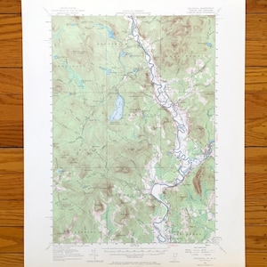 May include: A vintage topographic map featuring a detailed depiction of a geographical area. The map showcases a river, lakes, and elevation contours in shades of green, blue, and brown. The map is printed on aged paper.