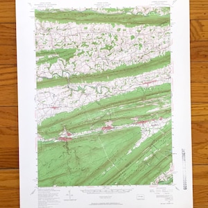Puede incluir: Un mapa topográfico detallado de una región montañosa, con áreas sombreadas en verde que representan bosques y cambios de elevación. El mapa incluye curvas de nivel, carreteras y nombres de lugares, impreso en papel blanco.
