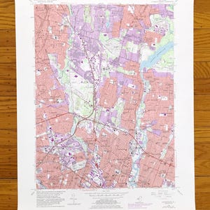 May include: A detailed topographic map showing roads, buildings, and natural features. The map uses pink, purple, green, and blue to represent different land types and elevations. The map is printed on white paper. Measurements are not included.