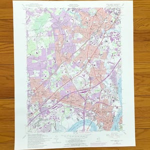 Può includere: Una carta topografica dell'United States Geological Survey di Perth Amboy, New Jersey, con dati cartografici dettagliati, zone codificate a colori rosa, viola e verde, reti stradali e corpi idrici stampati su un foglio di carta rettangolare bianco.