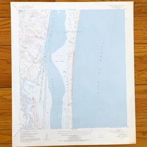 以下が含まれることがあります： 海岸線が描かれたヴィンテージ地形図。ベージュと緑色の陸地と、薄い青色のメキシコ湾が特徴です。詳細な等高線とテキストが含まれており、白い縁取りがあります。