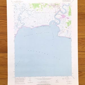 May include: A United States Geological Survey topographic map of the Port Norris quadrangle in New Jersey. The map features the Maurice River Cove and Delaware Bay in light blue, with surrounding land areas in white, green, and pink.