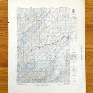 Può includere: Una mappa vintage di Perth, Canada, con dettagli topografici. La mappa presenta un reticolo, strade e corpi idrici blu. Il titolo "PERTH" è visibile in alto. La mappa è stampata su carta invecchiata.