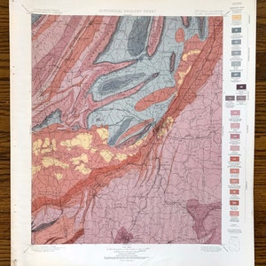 May include: A historical geology sheet map of Georgia and Alabama, showing the geological formations of the Appalachian Mountains. The map is color-coded with different shades of pink, red, yellow, blue, and green to represent different geological periods. The map also includes a legend with a key to the different colors and geological formations.