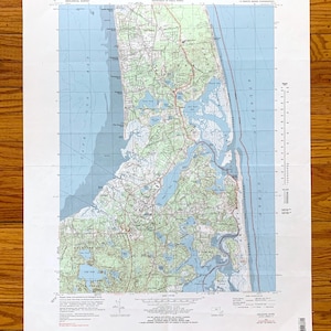Puede incluir: Un mapa topográfico vintage de Orleans, Massachusetts, que muestra la costa, las vías fluviales y las tierras circundantes. El mapa está impreso sobre un fondo azul claro con líneas verdes y marrones que indican las características del terreno. El mapa incluye el texto "UNITED STATES DEPARTMENT OF THE INTERIOR GEOLOGICAL SURVEY" y "COMMONWEALTH OF MASSACHUSETTS DEPARTMENT OF PUBLIC WORKS".