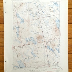 Pode incluir: Um mapa topográfico vintage do estado do Maine, mostrando a área ao redor das cidades de Greenville e Jackman. O mapa é impresso em papel cor de creme e apresenta linhas de contorno marrons, recursos hídricos azuis e linhas vermelhas que indicam estradas e trilhas. O mapa é intitulado "Estado do Maine, Domínio público, Pesquisa geológica, Mapa topográfico, 1952."