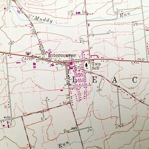 Op de afbeelding: Een vintage kaart met een rode lijn die er doorheen loopt. De kaart toont de stad Intercourse, Pennsylvania, met een school, een begraafplaats en een beek. De kaart toont ook de omgeving, inclusief wegen, rivieren en andere bezienswaardigheden.