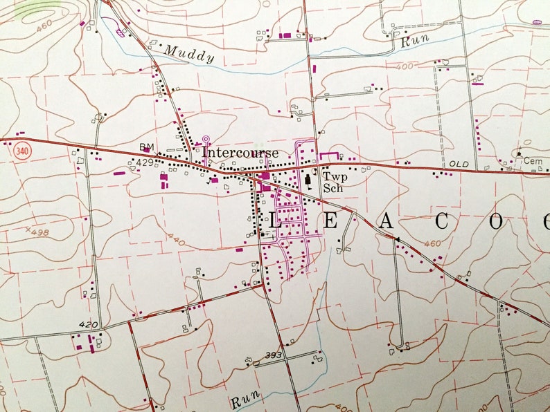 Op de afbeelding: Een vintage kaart met een rode lijn die er doorheen loopt. De kaart toont de stad Intercourse, Pennsylvania, met een school, een begraafplaats en een beek. De kaart toont ook de omgeving, inclusief wegen, rivieren en andere bezienswaardigheden.