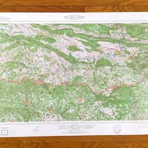 Puede incluir: Un mapa detallado de Blue Ridge Parkway, con colores verde, blanco y rojo. El mapa muestra la topografía del área, incluyendo montañas, ríos y carreteras. El título "Blue Ridge Parkway" es visible en la parte superior.