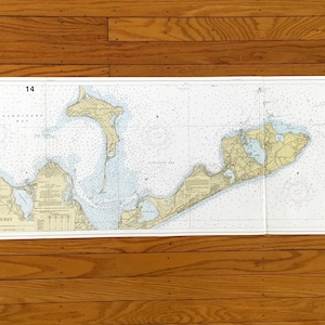 May include: A nautical chart of Gardiners Bay, featuring detailed depictions of the coastline, water depths, and navigational markers. The chart is printed on white paper and includes the number "14" in two corners. The map is laid out on a wooden surface.