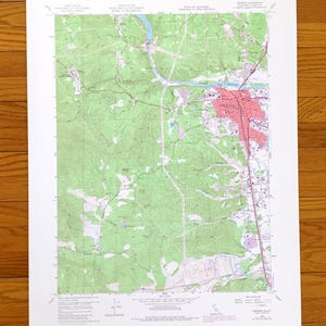 Pode incluir: Um mapa topográfico detalhado com áreas verdes, azuis e vermelhas. O mapa mostra uma paisagem com rios, estradas e uma cidade marcada a vermelho. O mapa é impresso em papel branco.