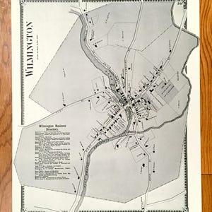May include: A vintage black and white map of Wilmington, featuring the Wilmington Business Directory. The map shows streets, buildings, and a river, with the city name at the top. The map is framed with a decorative border.