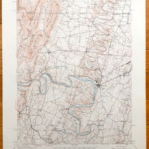 Puede incluir: Un mapa topográfico vintage del Cuadrángulo de Williamsport, Maryland, Virginia Occidental y Pensilvania. El mapa muestra el río Potomac serpenteando por la zona, con varias ciudades y carreteras marcadas. El mapa está impreso en papel color crema con líneas marrones y azules.