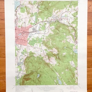 Puede incluir: Un mapa topográfico vintage del área alrededor de Pittsfield, Massachusetts, que muestra carreteras, ríos y cambios de elevación. El mapa está impreso en papel blanco con líneas y texto verde, marrón y azul. El mapa se titula "Pittsfield East Quadrangle" e incluye el texto "United States Department of the Interior Geological Survey" y "State of Massachusetts Department of Public Works".