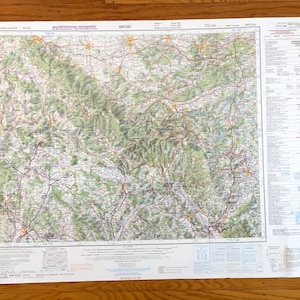 May include: A detailed map of a region in Western Europe, featuring a network of roads, towns, and topographical details. The map is printed on a large sheet of paper with text in the upper left corner that reads "Western Europe". The map is on a wooden surface.