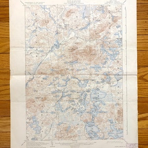 May include: Vintage topographic map of the Adirondack region in New York State, featuring detailed contour lines, lakes, and rivers. The map is printed in shades of brown and blue, with text indicating the area's geography and landmarks. The map is folded.