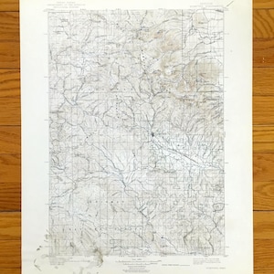 May include: A vintage topographic map with detailed contour lines, rivers, and place names. The map is printed on aged paper, showing signs of wear and tear. The map's color palette is primarily shades of gray and tan, with a grid overlay.