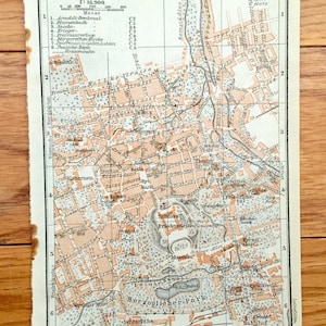 May include: A vintage map of Gotha, Germany, printed in black and white with red and orange highlights. The map shows the city's streets, parks, and landmarks, including the Schloss Friedenstein, the Herzoglicher Park, and the Bahnhof.