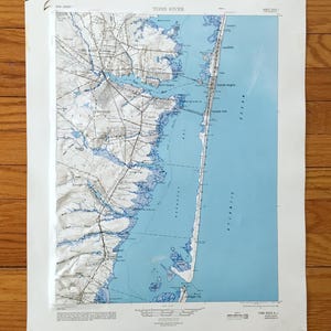May include: A vintage map of Toms River, New Jersey, showing detailed topographical lines in white and blue. The map depicts the coastline, waterways, and towns, with the Atlantic Ocean in light blue. The map is printed on aged paper.
