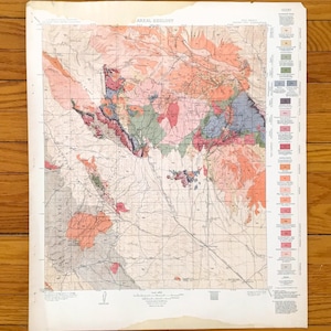 Puede incluir: Un mapa geológico antiguo con el título "AREAL GEOLOGY" en la parte superior. El mapa presenta una ilustración detallada de formaciones terrestres en tonos de rosa, verde, azul y marrón. Una leyenda está en el lado derecho. El mapa está en papel blanco con manchas.