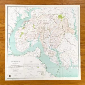 Puede incluir: Un mapa topográfico antiguo del condado de Charles, Maryland, con líneas de contorno detalladas, carreteras y vías fluviales. El mapa tiene una combinación de colores verde claro y beige, con el río Potomac en la parte inferior. El mapa está impreso en papel y doblado.
