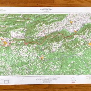 Puede incluir: Un mapa detallado de Blue Ridge Parkway, con colores verdes, blancos y rojos. El mapa muestra la topografía del área, con carreteras y otras características. El mapa está impreso en una hoja de papel blanca.