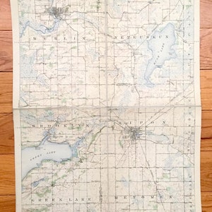 Puede incluir: Un mapa topográfico antiguo de una región con pueblos, lagos y ríos. El mapa plegado muestra nombres de lugares como Berlín, Ripon y Green Lake. El mapa tiene un patrón de cuadrícula y está impreso en tonos beige, azul y verde.