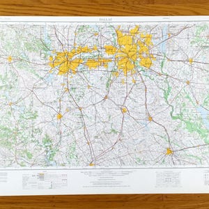 May include: A detailed map of Dallas, Texas, with yellow highlighting the city's urban areas. Roads and highways are shown in red and brown, with green areas representing parks and natural features. The map is printed on white paper.