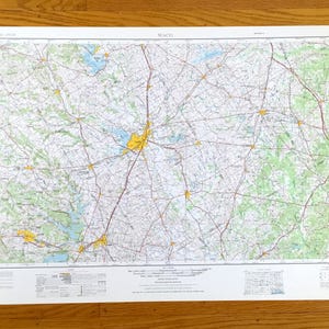 May include: A detailed map of Waco, Texas, showing roads, green areas, and water bodies. The map is printed on a white sheet with the word "WACO" at the top. The map is set against a wooden background.