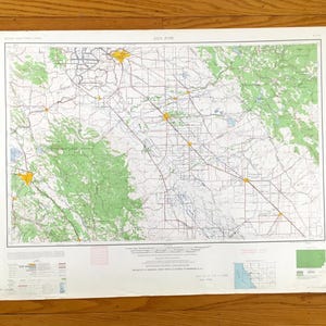 May include: A vintage map of San Jose, California, with detailed road networks, green shaded areas representing natural features, and yellow markers indicating urban areas. The map is printed on aged paper, showing signs of wear.