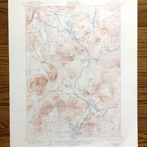 Könnte beinhalten: Eine Vintage-topografische Karte des Gebiets um Look Lake, NY, herausgegeben vom United States Department of the Interior Geological Survey. Die Karte zeigt die Lage von Bergen, Seen, Flüssen und Straßen in der Gegend. Die Karte ist in Schwarz, Braun und Blau auf weißem Papier gedruckt.