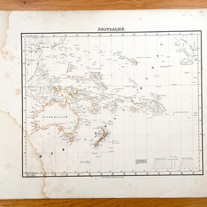 Op de afbeelding: Een antieke kaart van Australië uit 1850, gedrukt op papier met een rasterpatroon. De kaart toont de kustlijn van Australië, Nieuw-Zeeland en de omliggende eilanden. De kaart is getiteld "AUSTRALIEN" en bevat de tekst "Central Land" in het midden van de kaart.