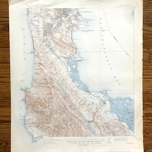 May include: A vintage map of San Francisco and San Mateo, California, showing the surrounding area, including the San Francisco Bay. The map is printed on paper and has a light blue and brown color scheme.