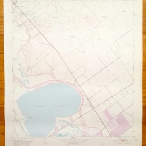 Peut inclure: Une carte vintage de Green Lake, Wisconsin, montrant le lac, les routes environnantes et les villes voisines. La carte est imprimée sur un fond blanc avec des lignes bleu clair et rose.
