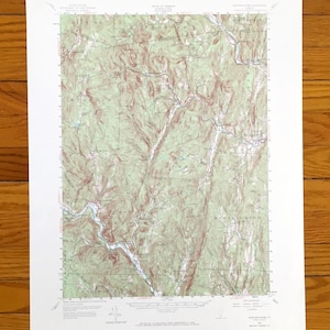 以下が含まれることがあります： 緑と茶色の等高線が特徴の、山岳地帯の詳細な地形図。 白い紙に印刷された地図には、地名とグリッド線が含まれています。 木の表面に置かれています。