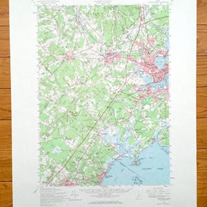May include: A detailed topographic map of the Portland, Maine area, featuring green forested areas, blue water bodies, and a network of roads and towns. The map includes the Atlantic Ocean and is printed on white paper.