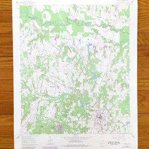 May include: A vintage topographic map with detailed contour lines, depicting a landscape with green forested areas, a river, and a town. The map is printed on white paper and is likely from the United States Geological Survey.