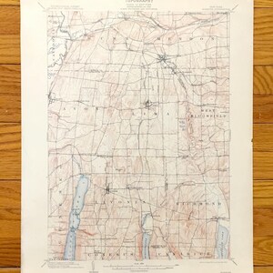 Puede incluir: Mapa topográfico antiguo de una región, con líneas de contorno detalladas, carreteras y nombres de lugares. El mapa está impreso en papel envejecido con una paleta de colores descoloridos, mostrando lagos y pueblos. El título "TOPOGRAFÍA" es visible en la parte superior.