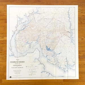 Puede incluir: Un mapa antiguo del condado de Charles, Maryland, que muestra la topografía y los distritos electorales. El mapa presenta una representación detallada de las características geográficas del condado, con tonos azules y marrones. El texto incluye "Mapa del condado de Charles".