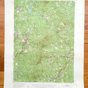 May include: A vintage topographic map of the Peterborough quadrangle in New Hampshire. The map shows the terrain, rivers, lakes, and roads in the area. The map is printed on paper and has a green and brown color scheme.