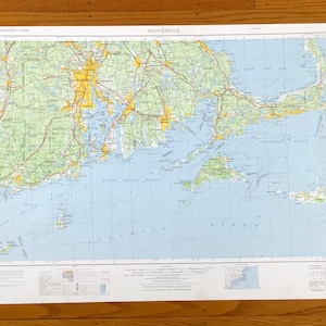 Può includere: Una mappa dettagliata di Providence, Rhode Island, e delle aree circostanti. La mappa presenta un oceano azzurro, masse terrestri verdi e aree urbane evidenziate in giallo. Sono visibili strade e autostrade, con la parola "PROVIDENCE" in alto.