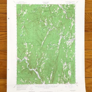 以下が含まれることがあります： バーモント州サクストンズリバー地域のヴィンテージ地形図。緑と白の地形の詳細が特徴です。地図には、ウィンダムやアテネなどの地名、縮尺、等高線が含まれています。紙はわずかに古びた外観をしています。