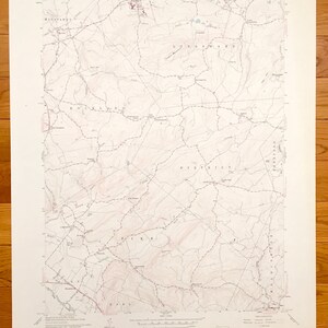 May include: A vintage topographic map of a rural area, featuring contour lines, roads, and place names. The map is printed in shades of brown and red, with text indicating the map's origin and scale. The map is on a white background.